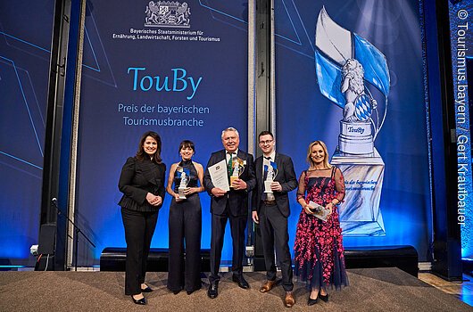 Staatsministerin Michaela Kaniber mit den drei Siegern des Tourismuspreises und der Moderatorin der Preisverleihung