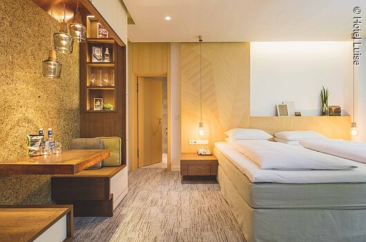 Ein Doppelzimmer in warmen Licht mit holzlastigen Interieur.