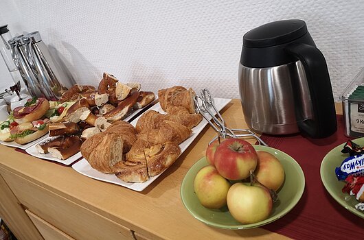 Verpflegung bei gemeinsamen Austausch von BayTM und TVF, Nürnberg Ein Tisch mit Croissants, belegten Brötchen, Brezeln, Äpfeln, einer Thermoskanne und Teebeuteln.