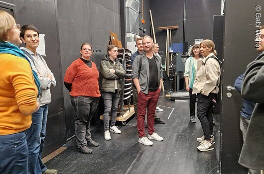 Besichtigung des Neubaus des Mainfranken Theaters durch Mitarbeitende des Tourismusverbandes Franken im Oktober 2025, Würzburg Gruppe von Menschen steht in einem Raum mit schwarzem Boden und Wänden, einige lächeln.