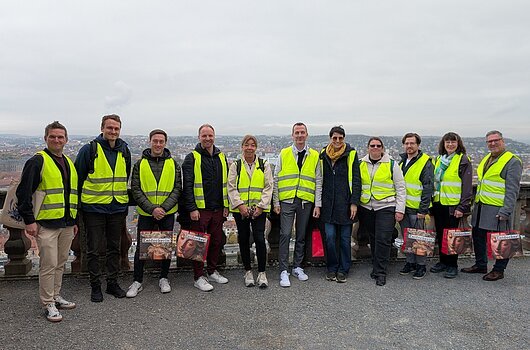Produktschulung für Mitarbeitende des Tourismusverbandes Franken. Würzburg Gruppe von Personen in gelben Warnwesten steht vor einer Stadtlandschaft.