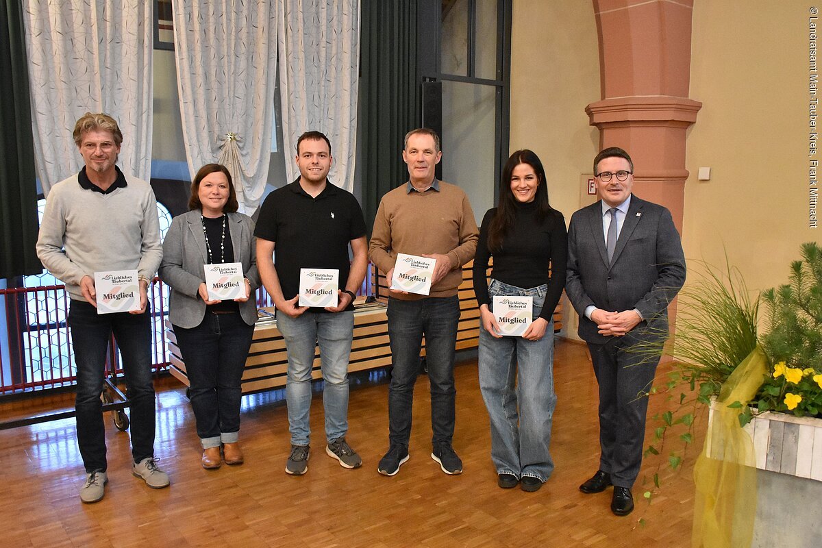 Aushändigung der Mitgliedschilder bei der Mitgliederversammlung 2025 des Tourismusverbandes "Liebliches Taubertal" Sechs Personen stehen nebeneinander in einem Raum, fünf halten Plaketten mit der Aufschrift „Mitglied“.