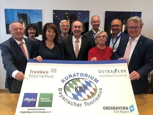 Neun Personen stehen hinter einem großen Banner mit Logos und Schrift zu bayerischem Tourismus.