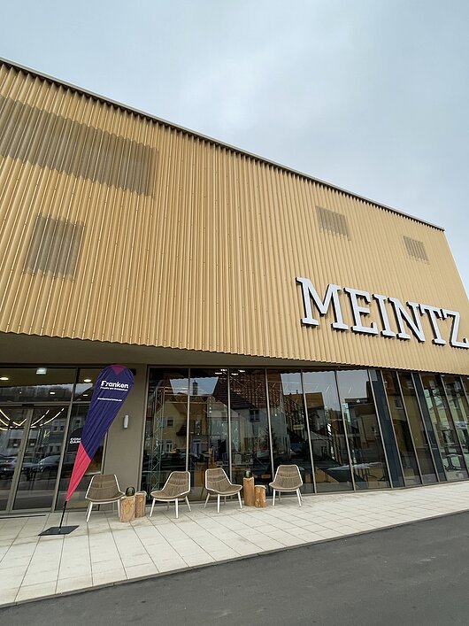 Pressegespräch 2026 im Hotel Meintz (Ochsenfurt, Fränkisches Weinland) Fassade eines Gebäudes mit großen Fenstern, Stühlen davor und Schriftzug „MEINTZ“ auf der Wand.