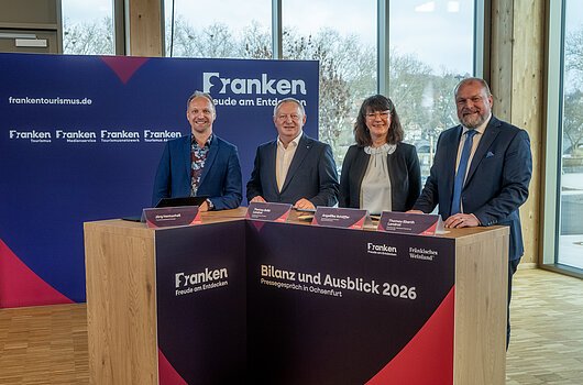 Vier Personen stehen an einem Holztisch mit Beschriftung „Bilanz und Ausblick 2026“ bei einer Pressekonferenz in Ochsenfurt.