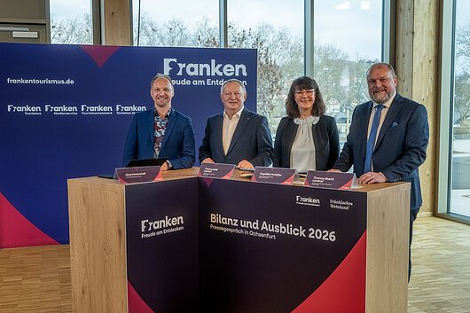 Pressegespräch 2026 (Ochsenfurt, Fränkisches Weinland) Vier Personen stehen an einem Holztisch mit Beschriftung „Bilanz und Ausblick 2026“ bei einer Pressekonferenz in Ochsenfurt.