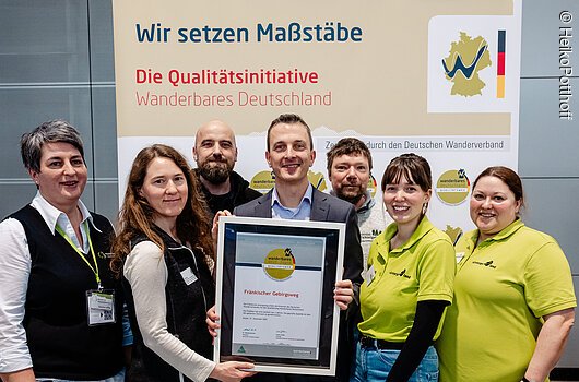 Sieben Personen stehen vor einem Banner der Qualitätsinitiative Wanderbares Deutschland und halten eine Urkunde für den Fränkischen Gebirgsweg.