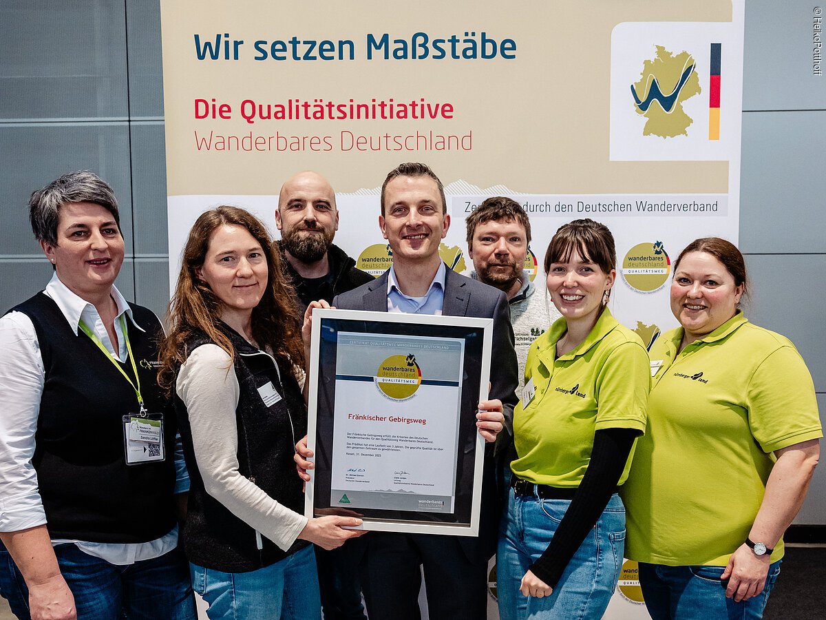 Sieben Personen stehen vor einem Banner der Qualitätsinitiative Wanderbares Deutschland und halten eine Urkunde für den Fränkischen Gebirgsweg.
