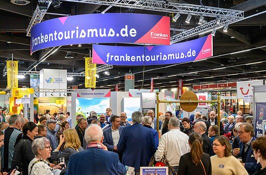 Franken-Stand bei der Freizeit-Messe Nürnberg 2026 Messehalle mit vielen Menschen vor einem Stand mit blau-rotem Banner „frankentourismus.de“ und gelben Fahnen „Naturpark Altmühltal“.
