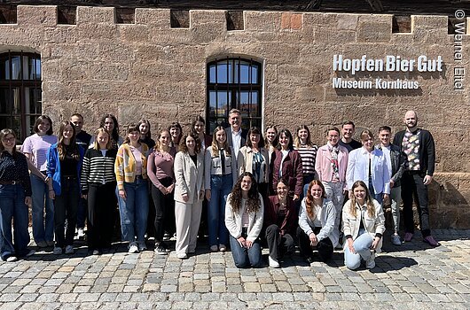 Gruppenfoto von 28 Personen vor einem Gebäude mit der Aufschrift „Hopfen Bier Gut Museum Kornhaus“.