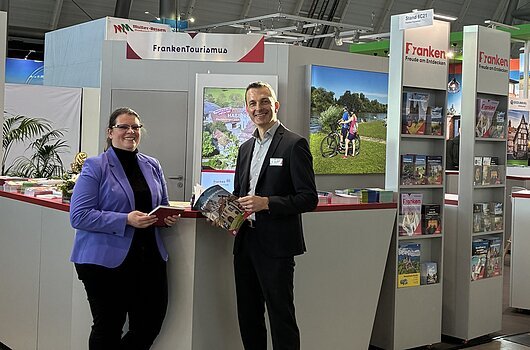 Messestand des Tourismusverband Franken mit zwei Personen, Informationsmaterial und Werbebannern in einer Halle