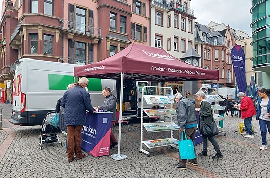 FrankenTour 2026, Frankfurt am Main Informationsstand mit rotem Zelt und Broschüren auf Pflasterstraße vor Altbauten, mehrere Personen schauen sich um.