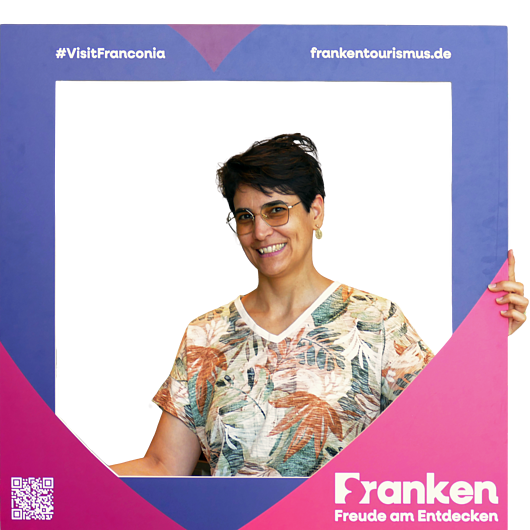 Karolina Klemm, Team FrankenTourismus Frau mit kurzen dunklen Haaren und Brille hält lila und pinken Fotorahmen mit Text zu Franken-Tourismus.
